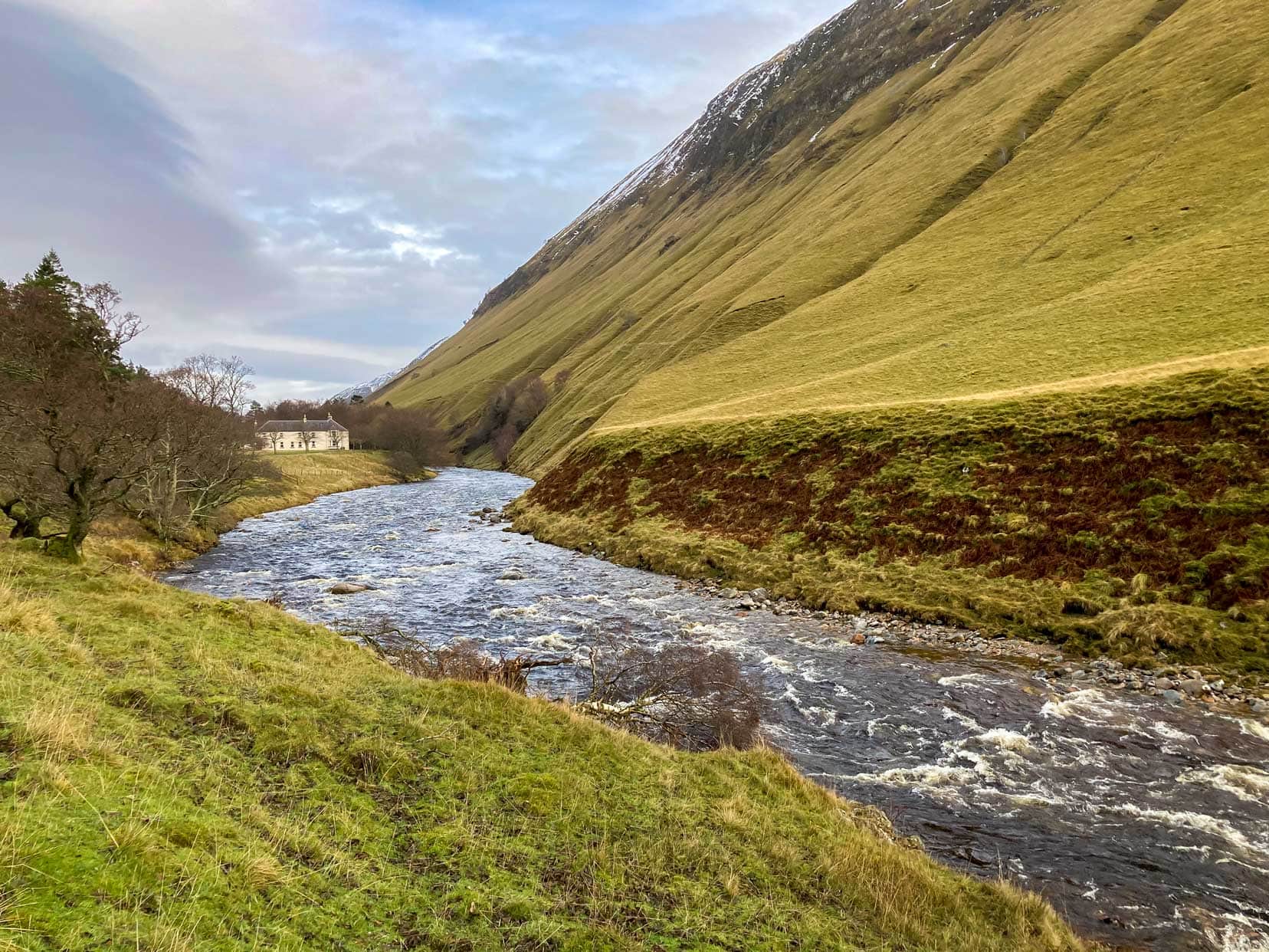 Cairngorms stream and white house at the foot of green mountains