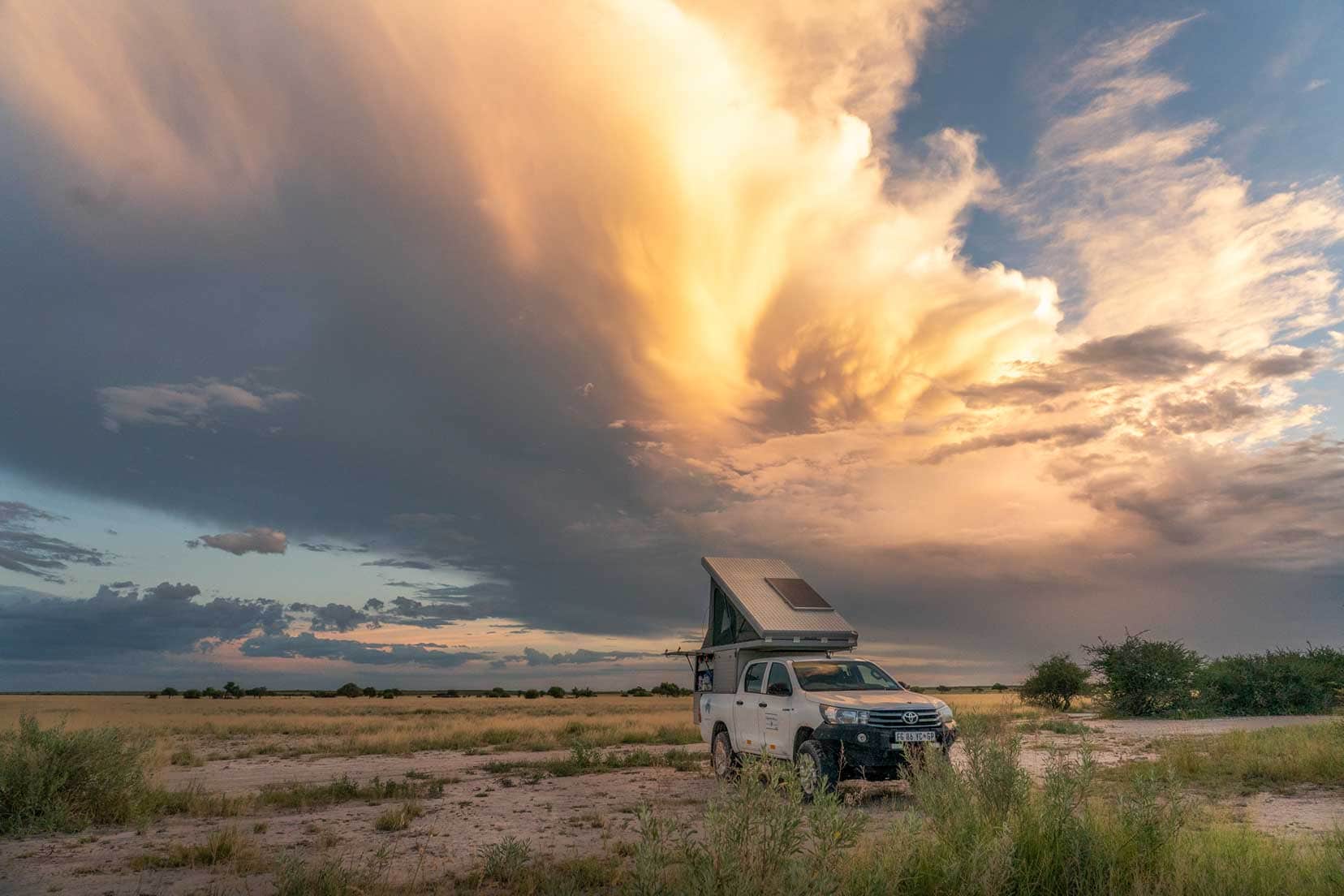 Hilux 4x4 with roof top tent on a pan in Botswana with the sunset illuminating the clouds