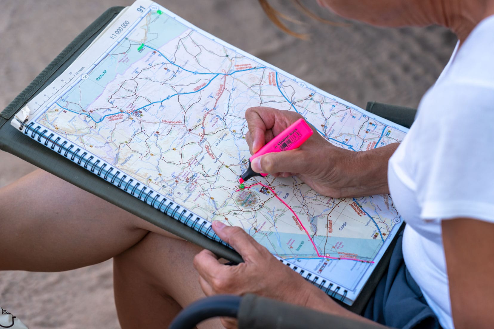 a lady tracing a line on a large road map that is placed on her lap with a coloured marker 