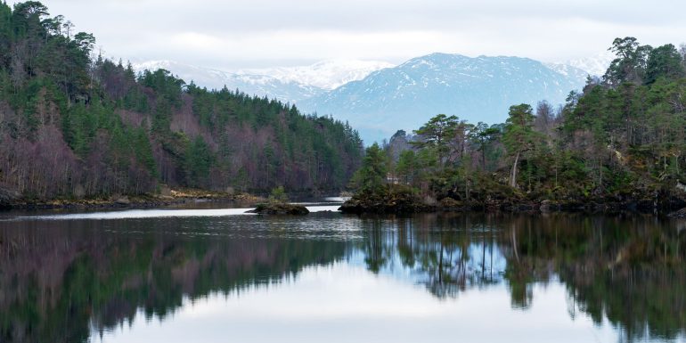 Scenic view of Glen Affric with a still lake mirroring the snowy mountains and pine tress in the background