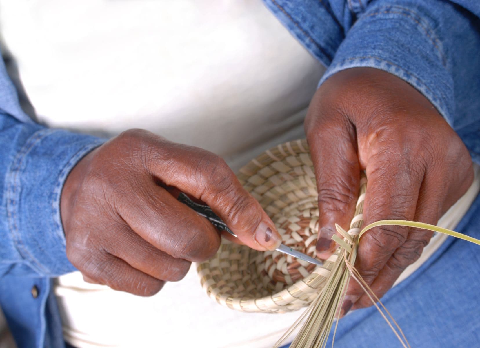 dark skinned woman hands weaving a basket with dried grasses