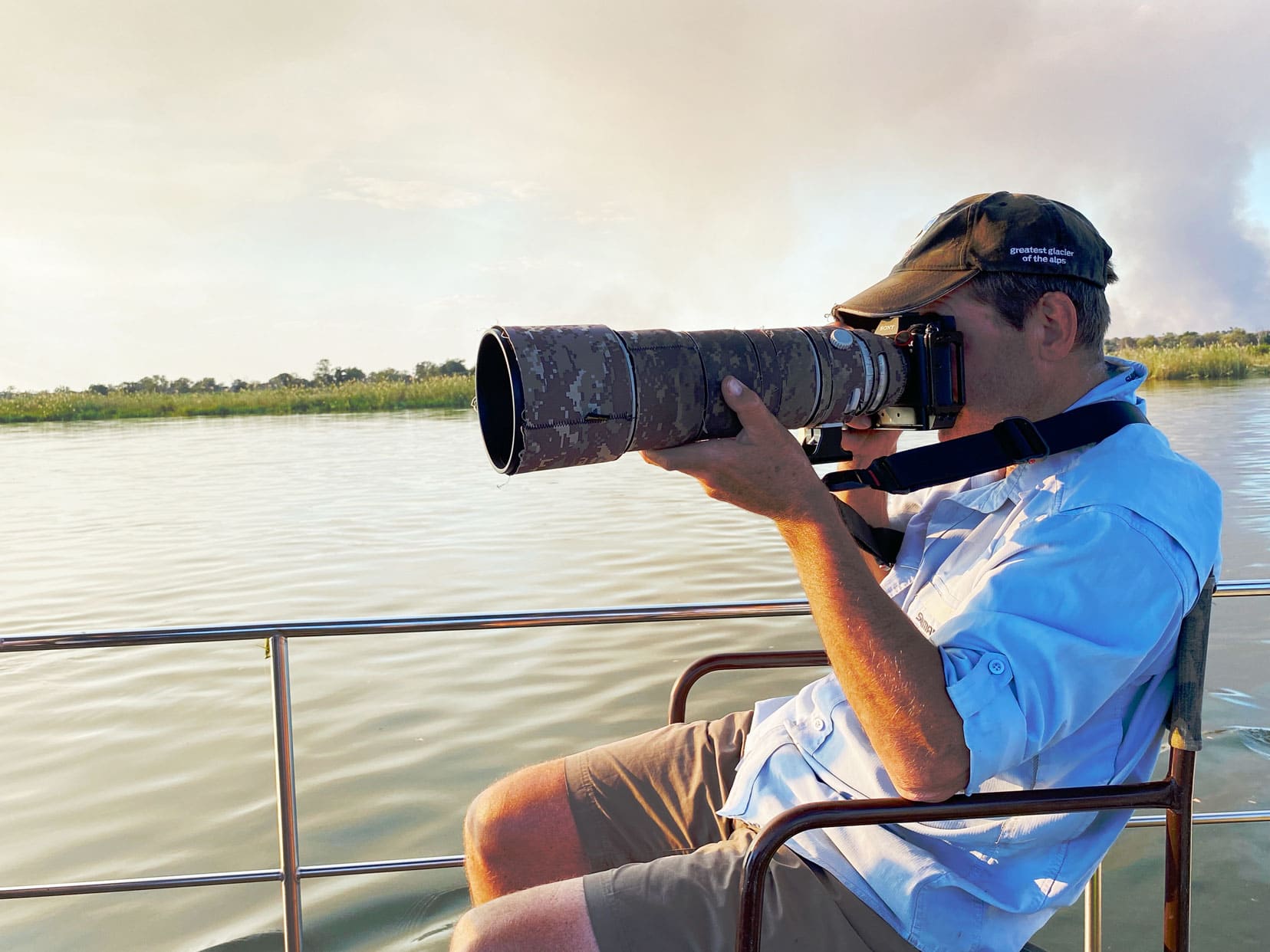 Lars sat on a boat on the okavango river taking a phot with a large lens on his camera