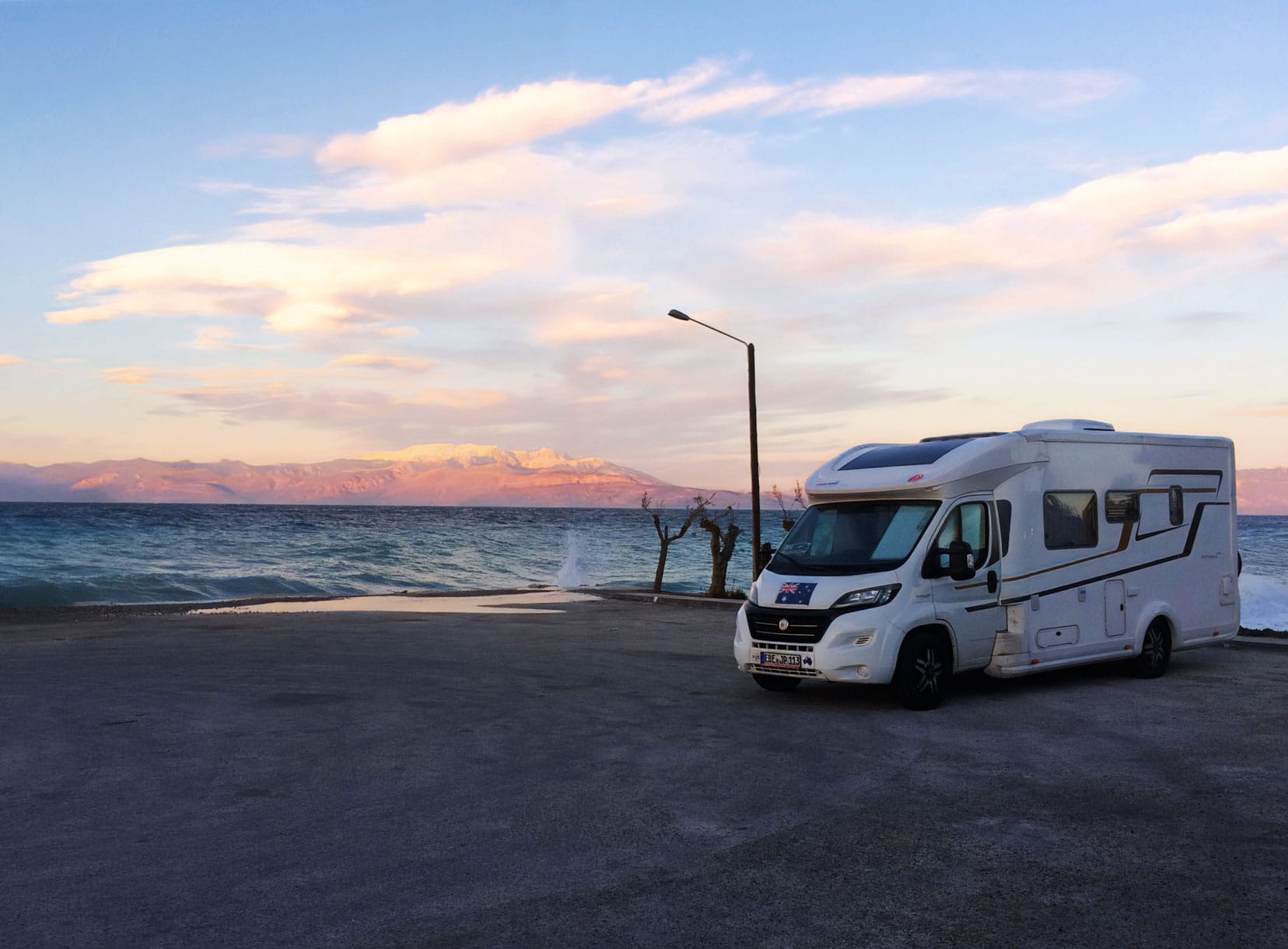 motorhome parked by the ocean with a pink sunset on the mountains in the background