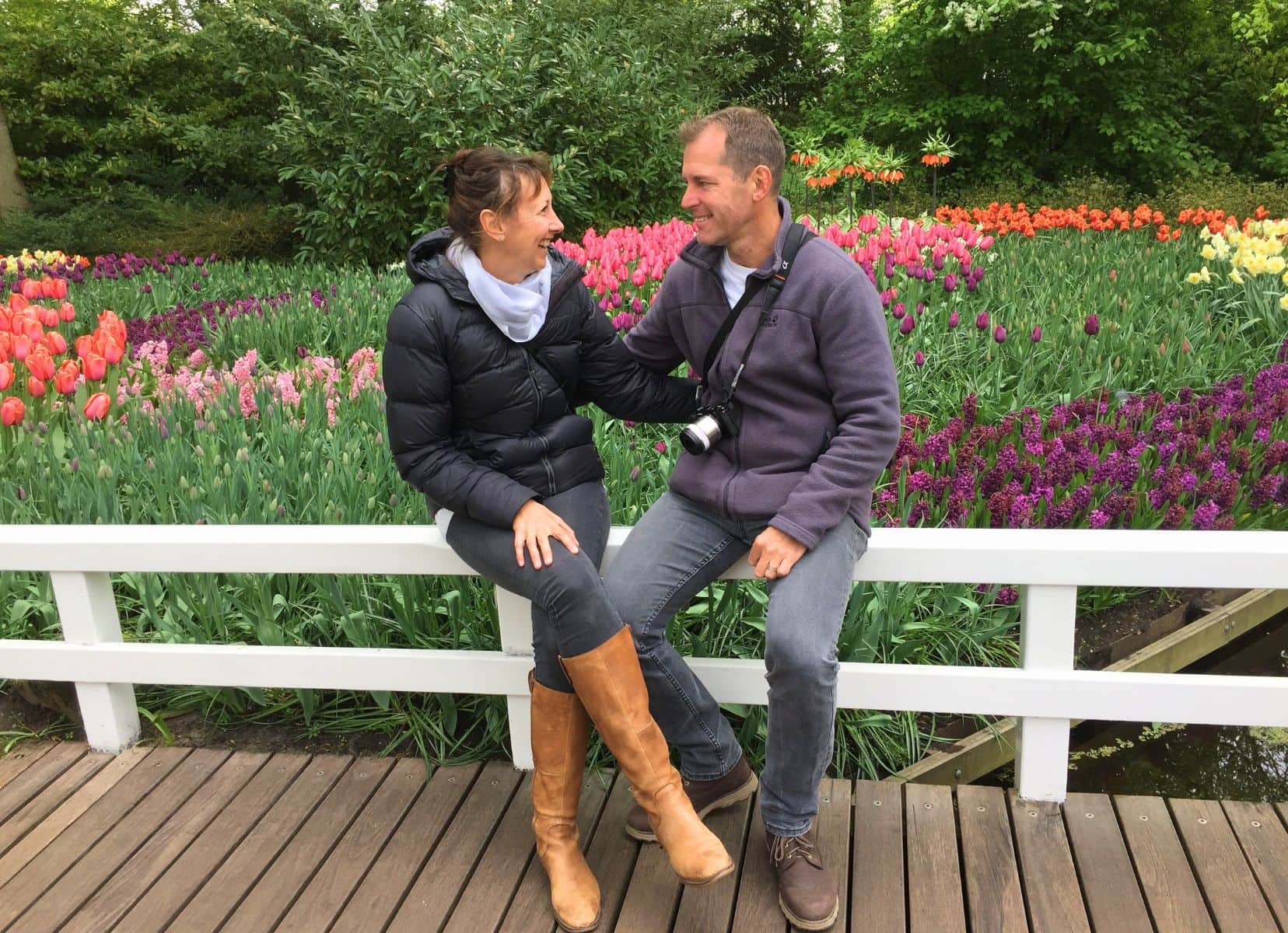 Lars and shelley sat laughing with field of tulips behind them - laughing together is one of our travel tips for couples. 