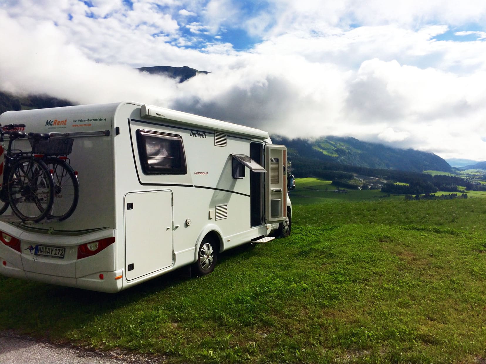 motorhome parked on a green hill with mountains in the background