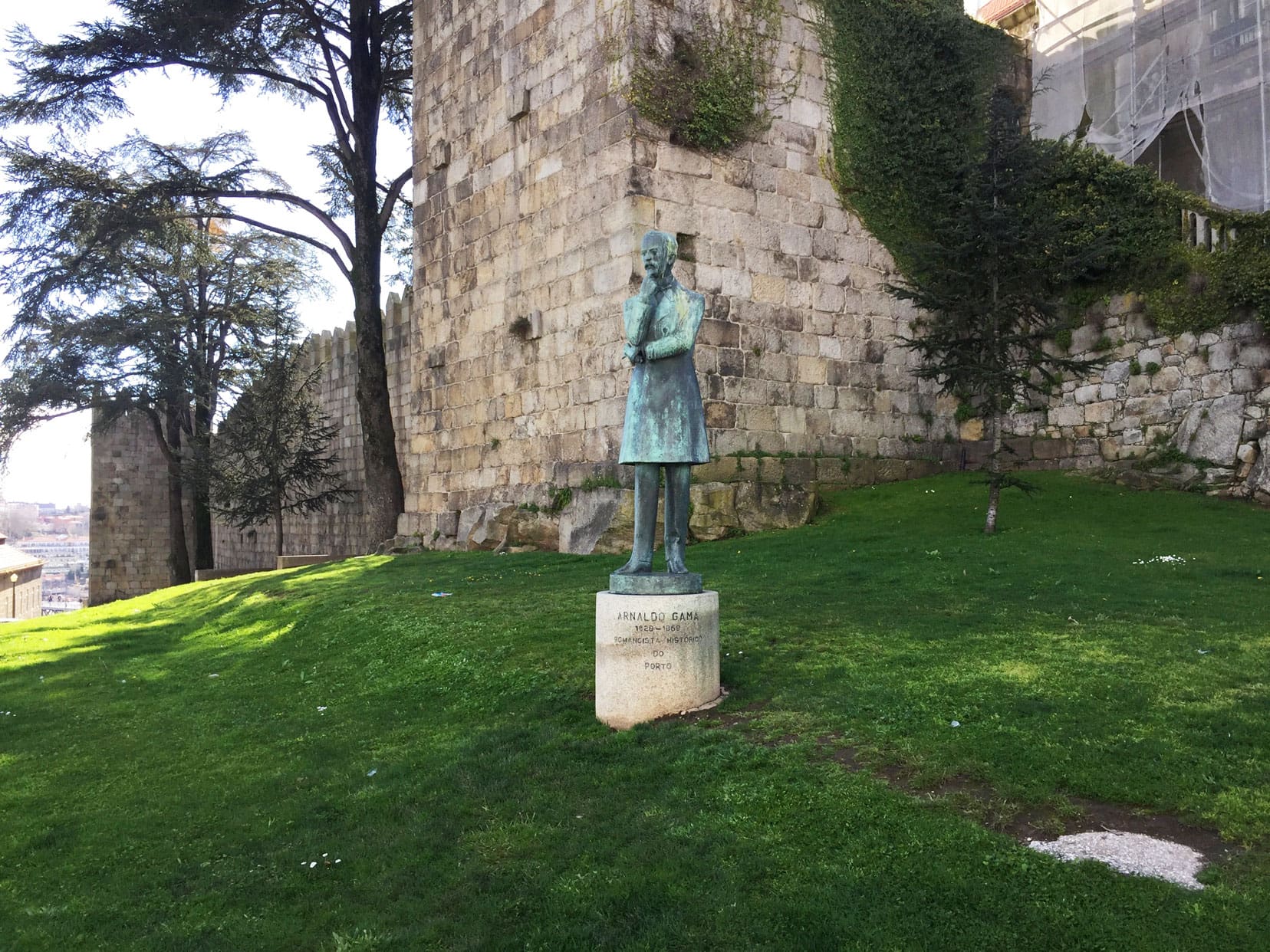 Bronze statue of Arnaldo Do Gama a Portuguese writer situated on a grassy bank in front of the medieval city walls