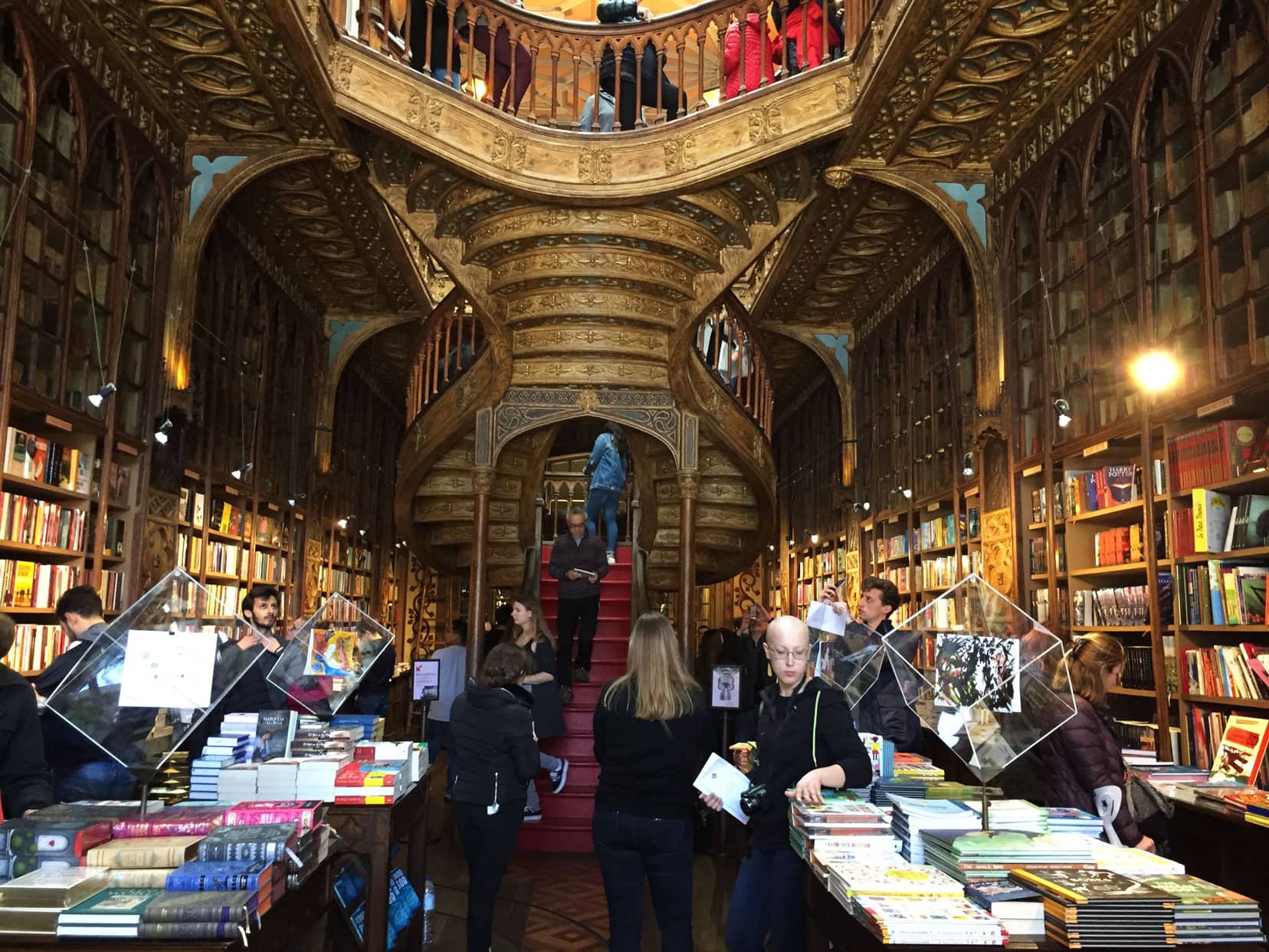 inside the Livraria lello bookshop with a double spiral red staircase and wood coloured intricate carved patterns in the artraves 