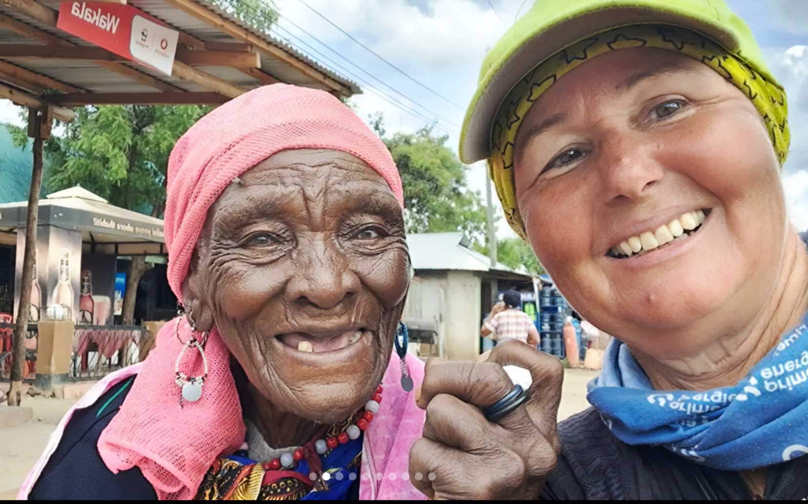 Anna with a bicycle helpmet on beside a smiling dark skinned woman wiuth a pink headscarf, lon earings and several teeth missing