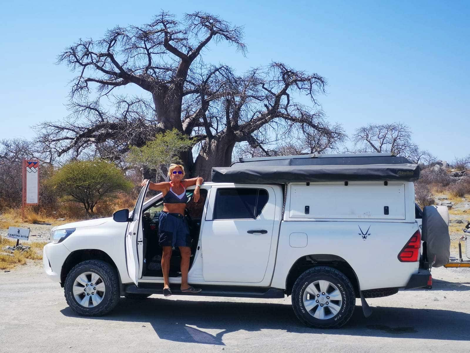 Christine-at-Baines-Baobabs stood on the sidestep of her 4x4 with a baobab tree in the background 