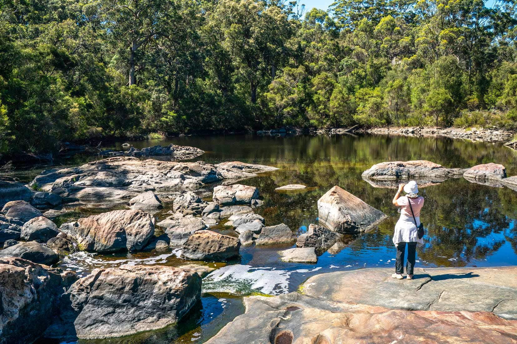 Shelley taking photos at Circular Pool - a serene pool with granite rocks scattered inside it and a backdrop of trees