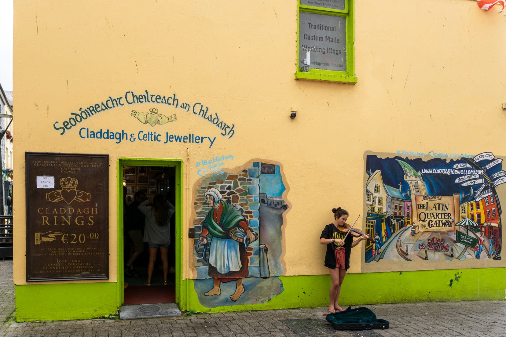 Violinist in a Galway Street by a yellow wall with murals painted on it