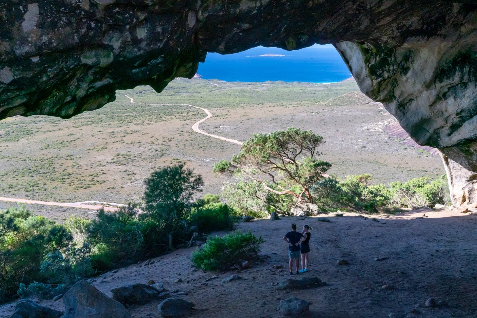 A couple stood Inside the cave with views of the ocean and capeLe grand