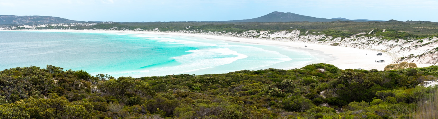 Panorama of Wharton Beach - white sand, blue ocean with low greenery bushland on the shore