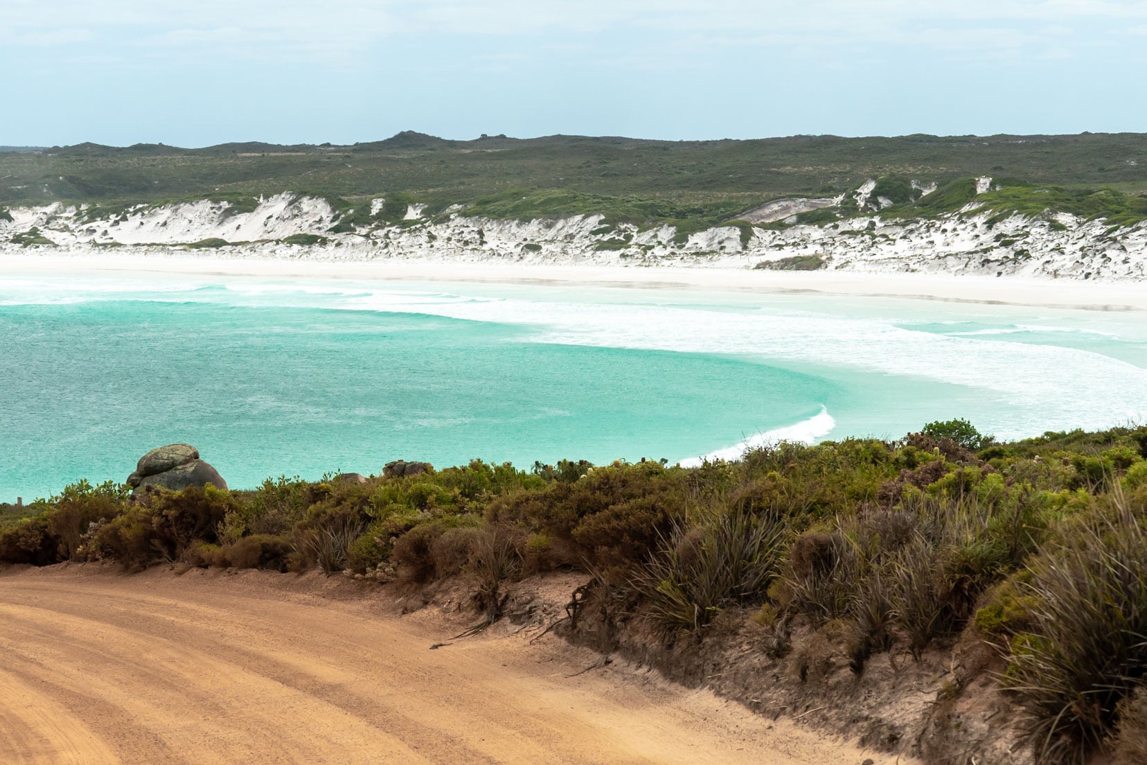 Heading towards Wharton Beach with sandy gravel track on the road and clear turquoise waters and white sandy arched bay