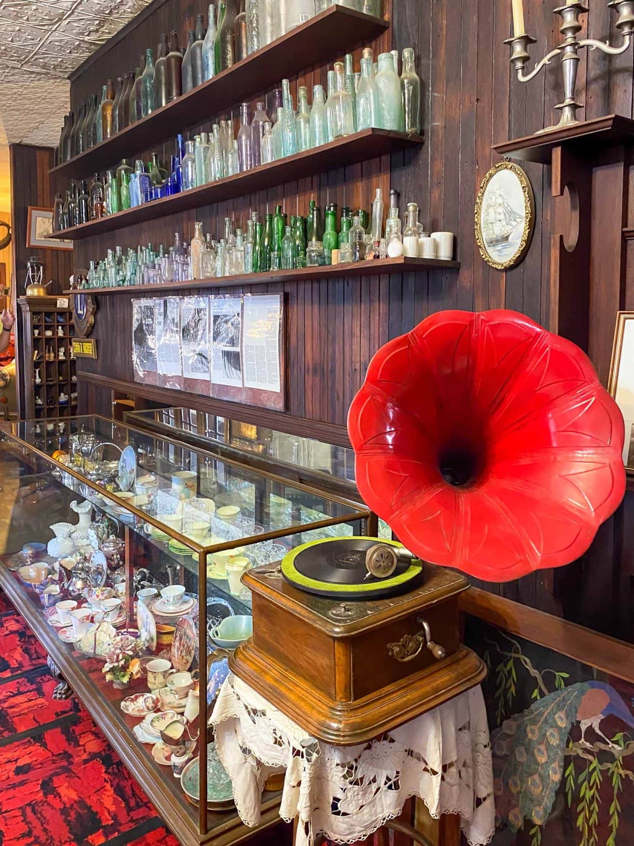 A gramphoe with a big red speaker and a shelf with old bottles and momentoes on it