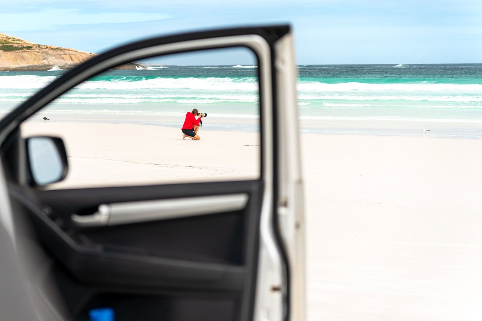 CAr door open with image of shelley taking a photo on the white sand beach 