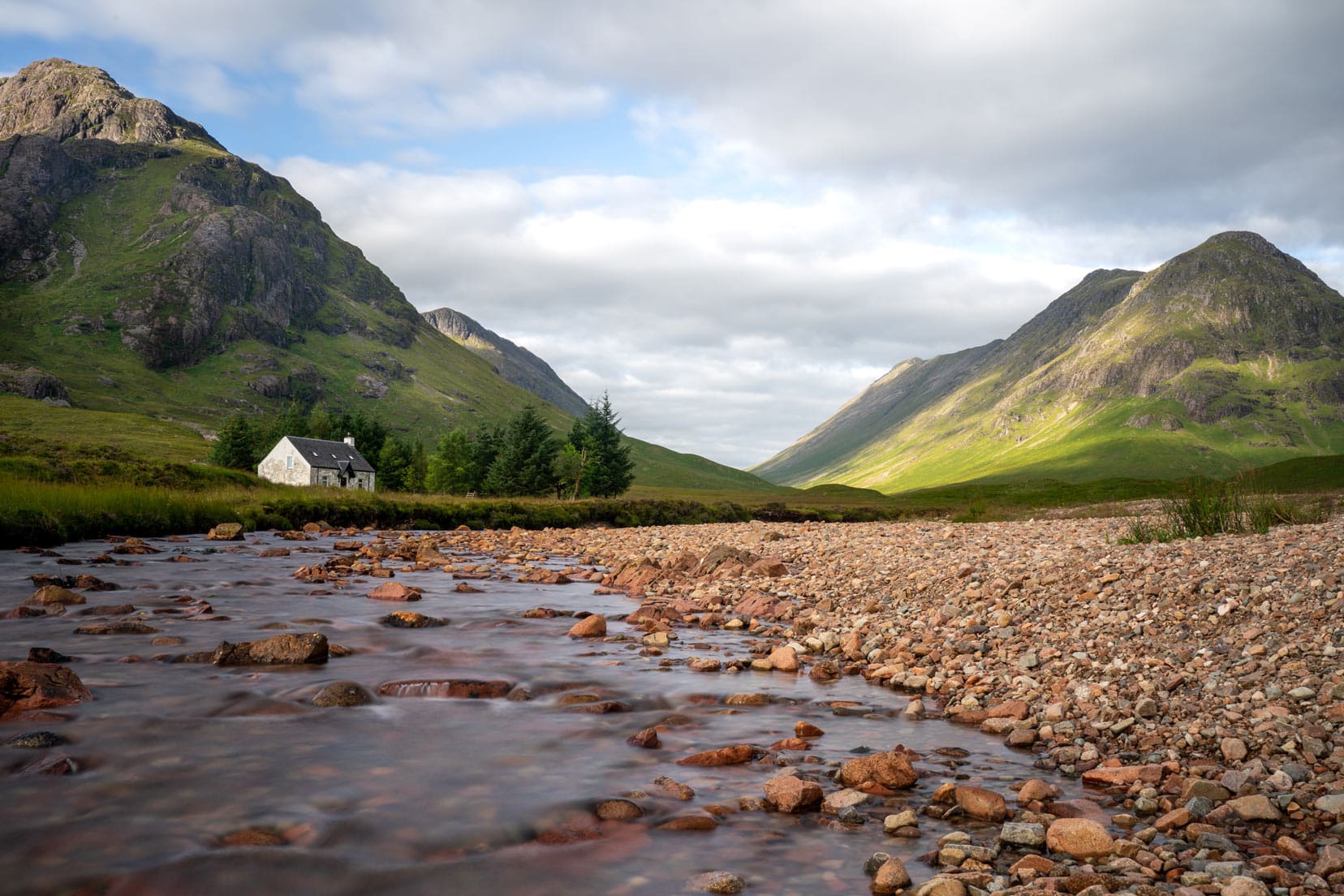 Glencoe long exposure with blurred river over brown pebbles and green mountains in the background