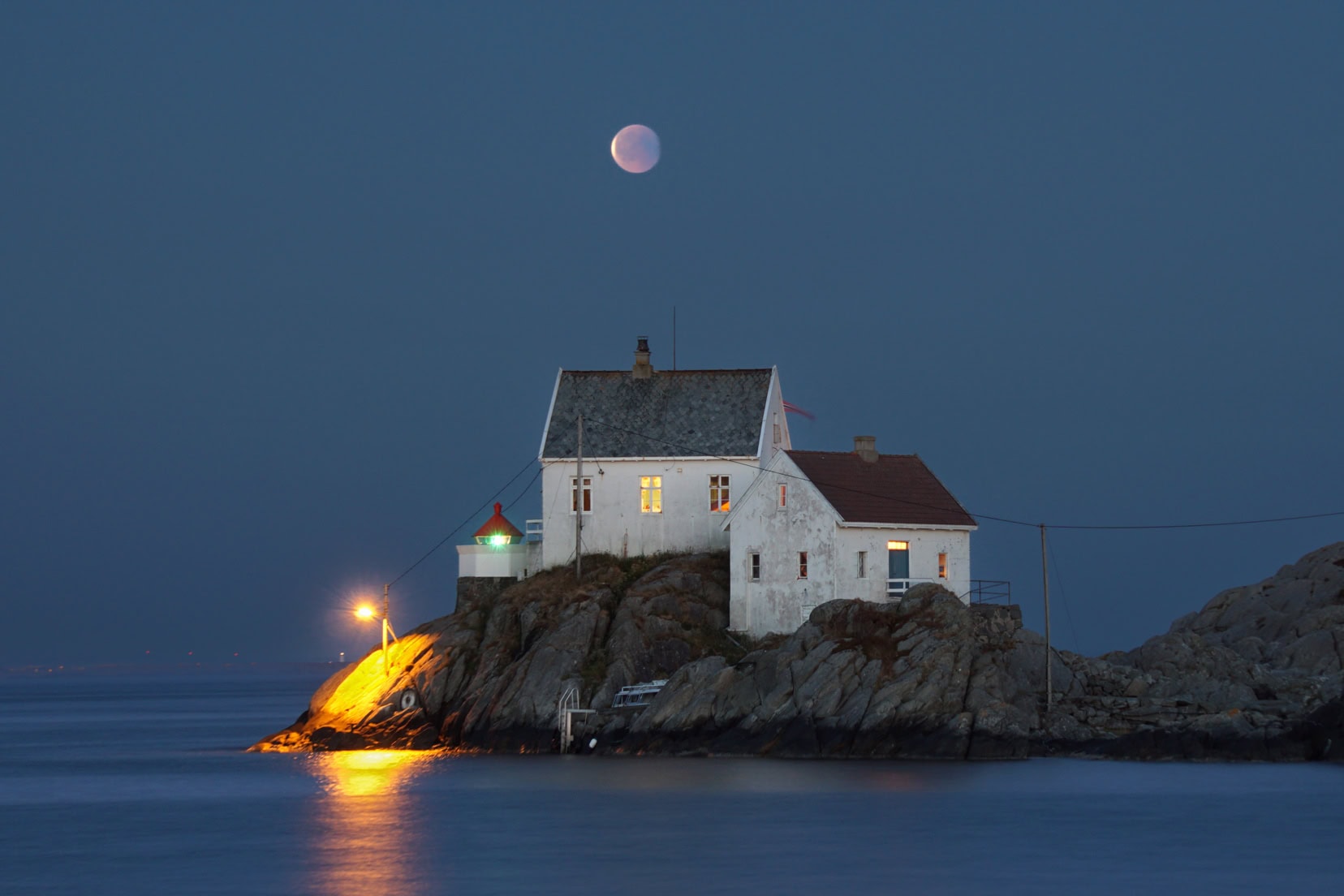 blood moon norway rising over a white building on rocks in the ocean