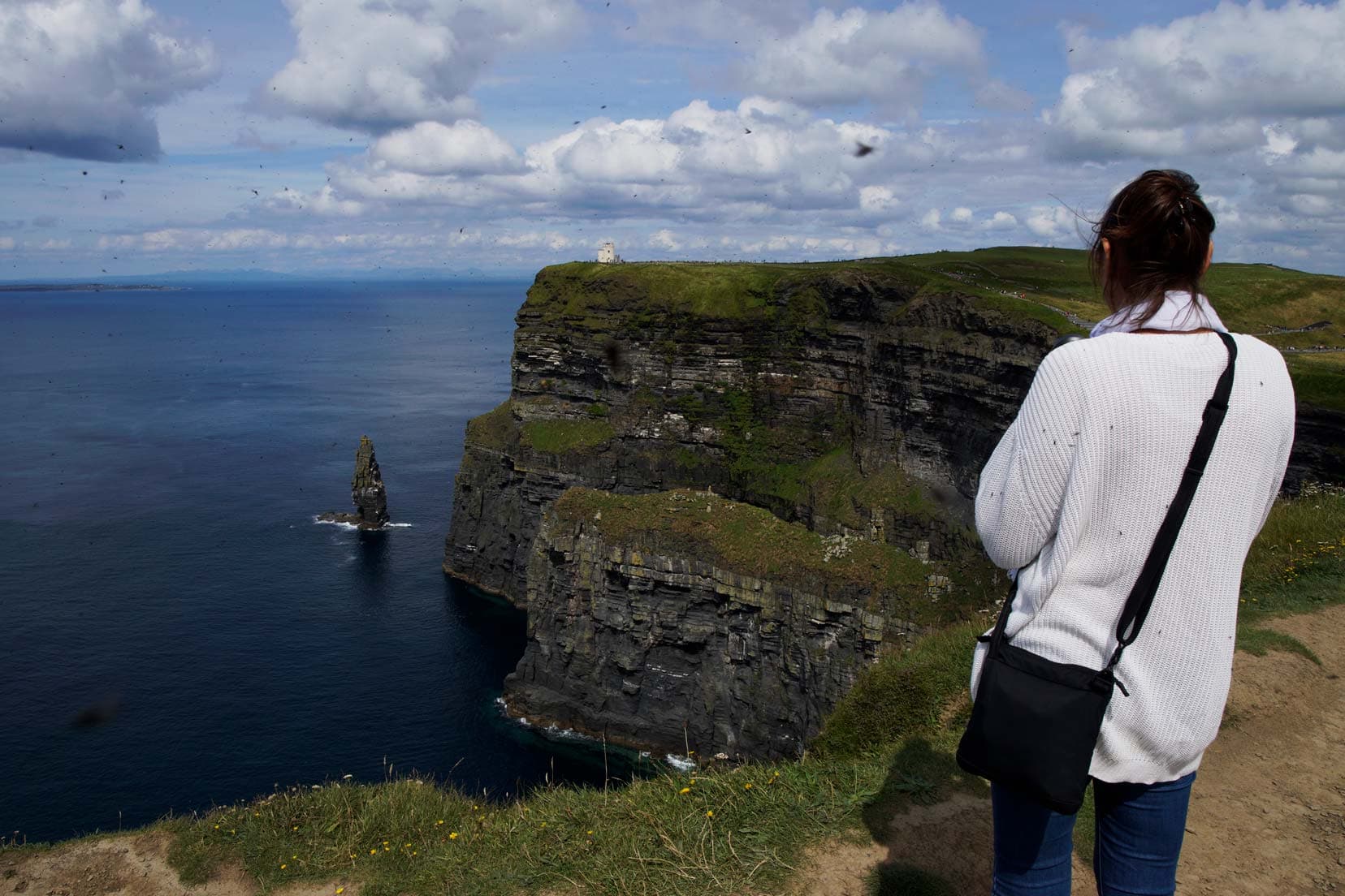 Black-bag-and-shelley in-Ireland stood by hte edge of the cliff with views of the ocean and rugged cliff faces along the coast