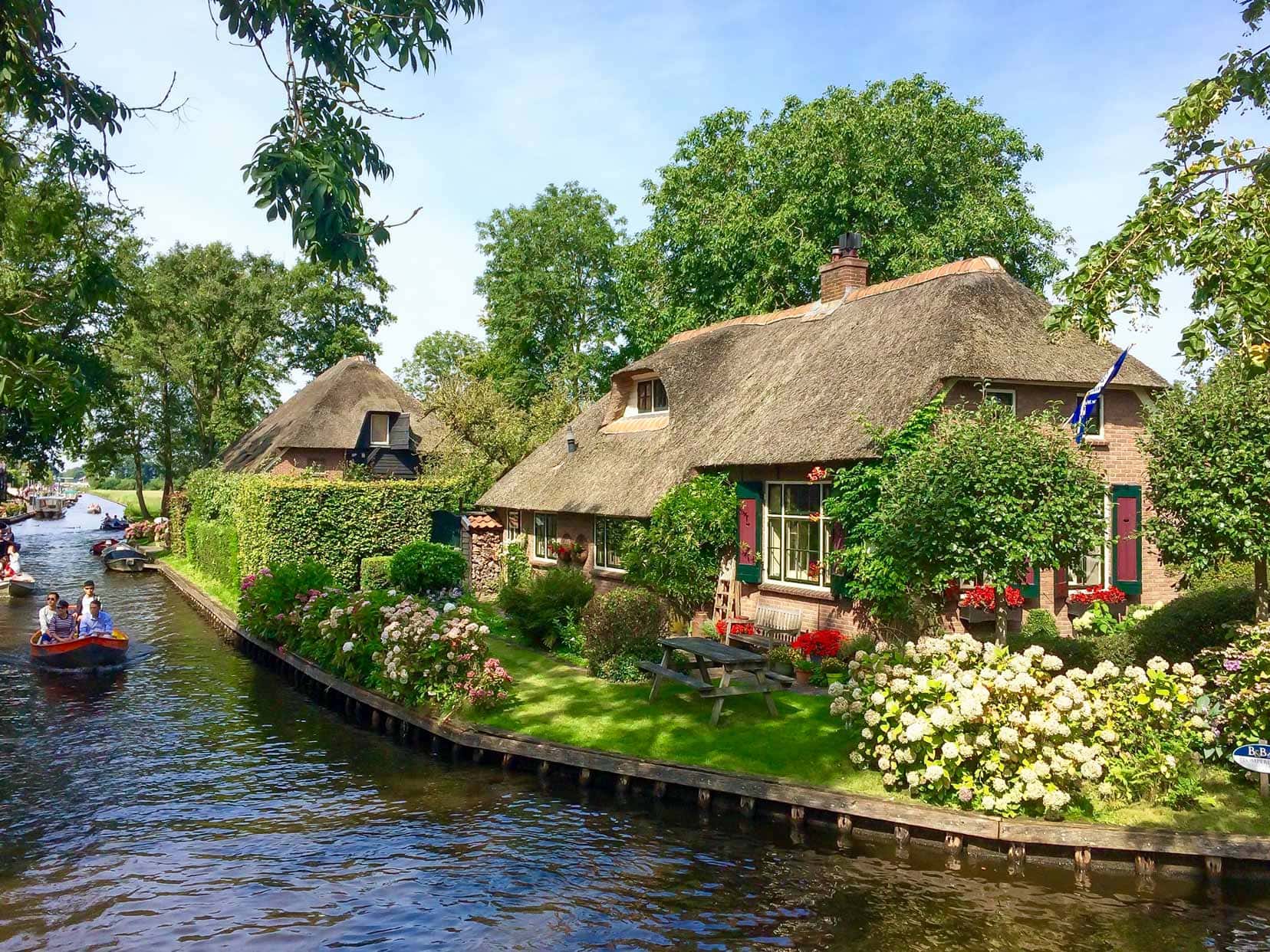Pretty thatched cottage on the banks of a small canal with lots of flowers and bushes growing around it 