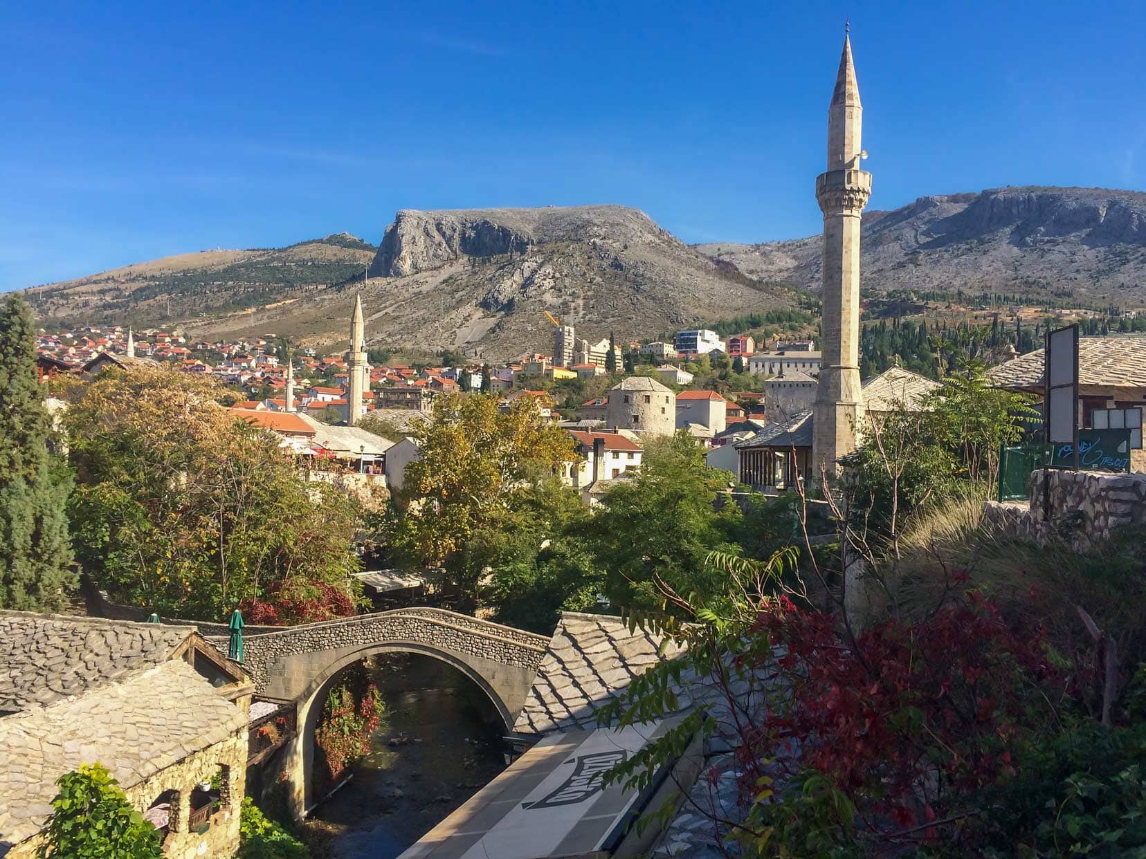 Mostar in Bosnia, a stone bridge in the foreground and minarets in the back ground with a bak drop of craggy mountains