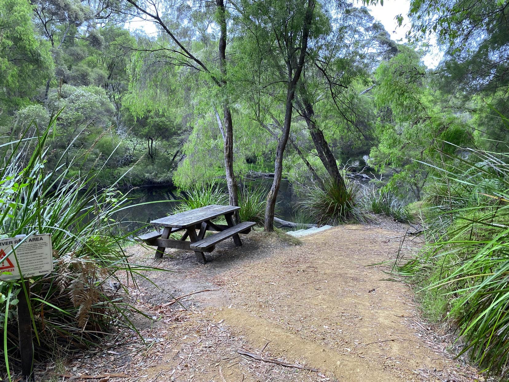 Blackbutt stop with a wooden picnic table and steps leading into the river. All surrounded by trees.