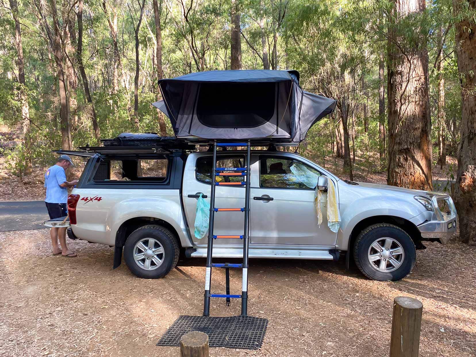 Honeymoon-Pool-Isuzu with rooftop tent and lars stood at the back of the car. Surrounded by trees 