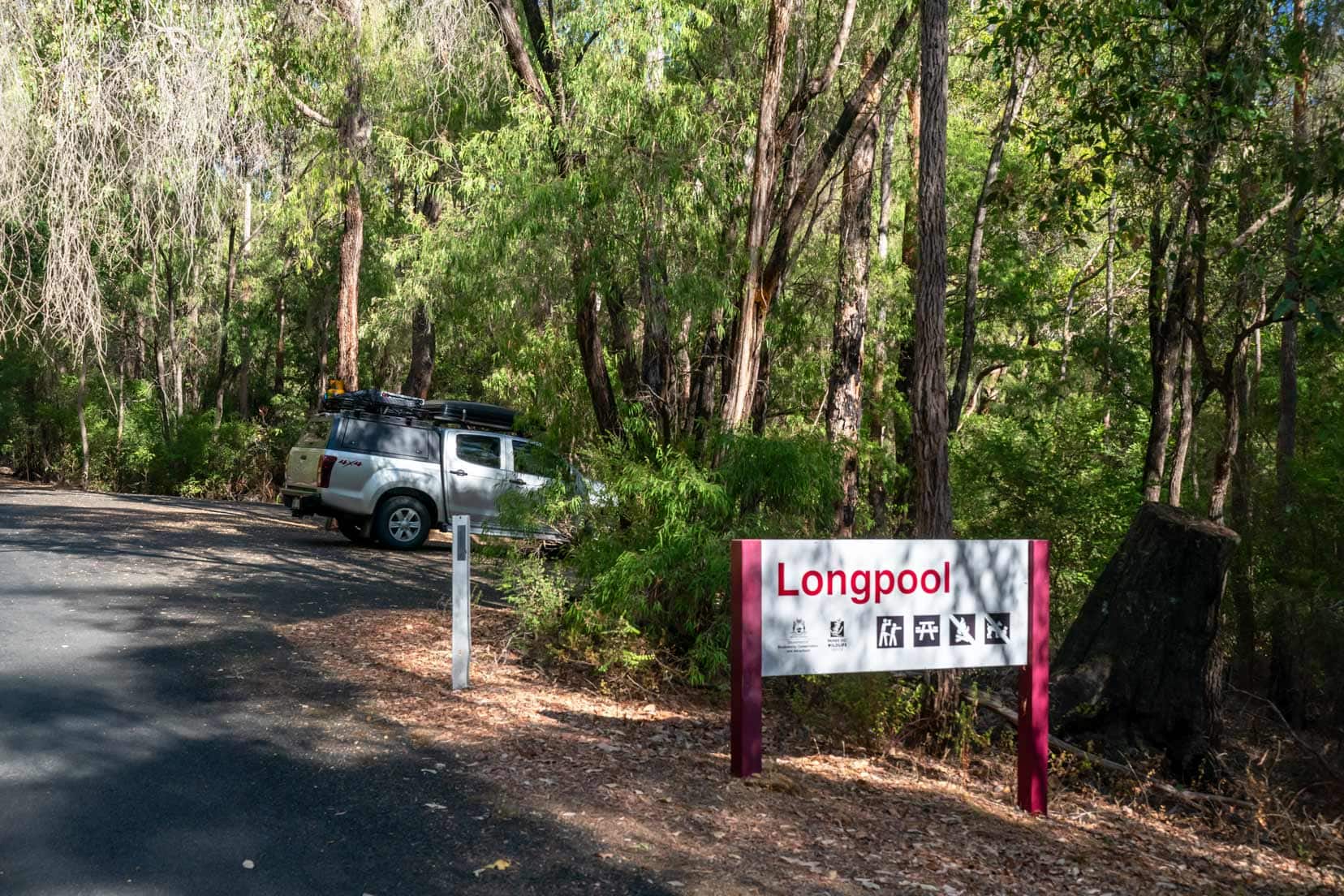 Sign for Long Pool with a car parked in a small pullout beside a narrow road flanked by tall trees.