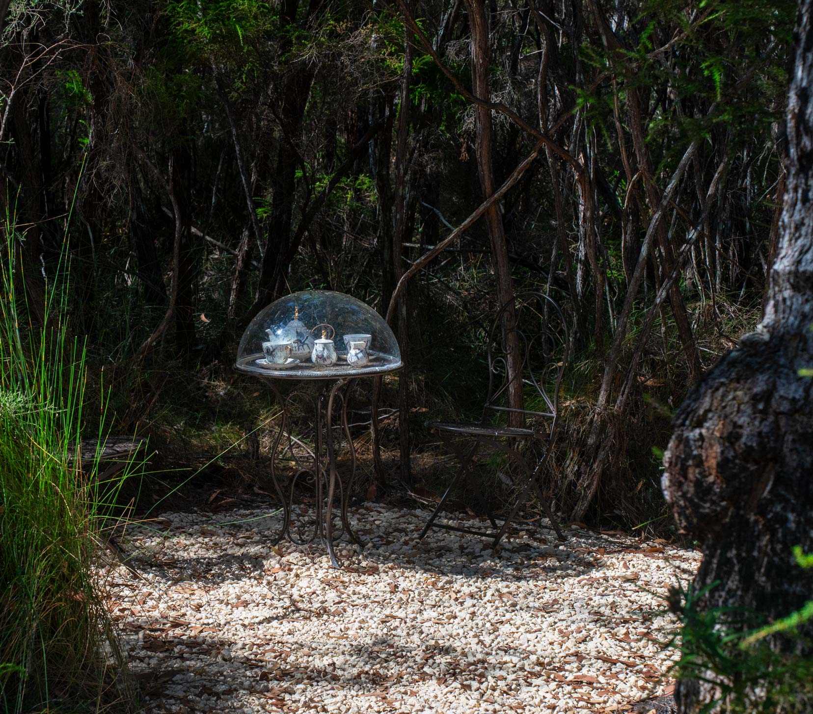 Tea set under a clear dome placed on a circular iron wrought table 