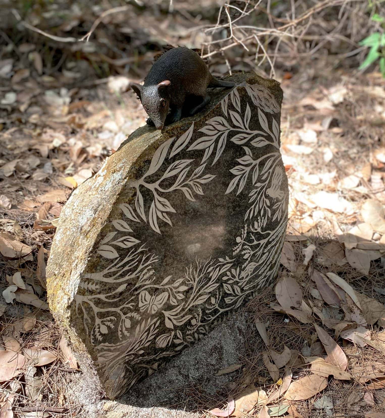 Stone with etched leaves abd a small mouse like creature on the top of the  stone