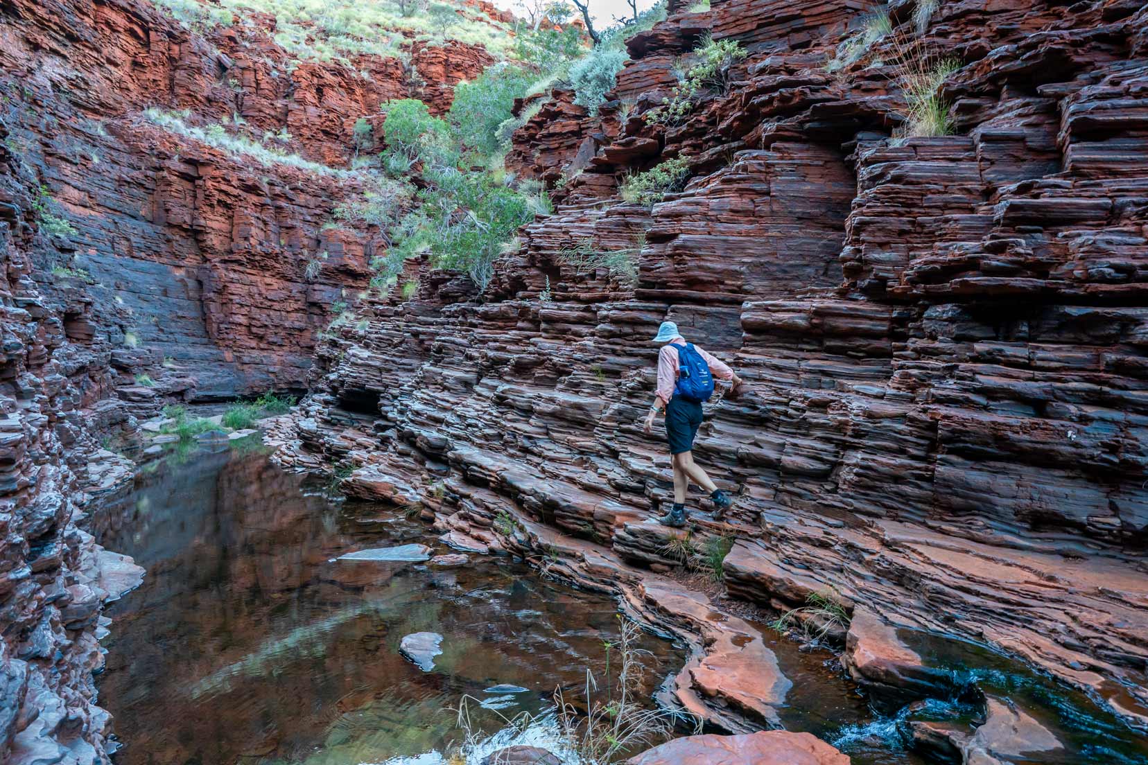 Shelley clambering along the rocks above the water in hancocks gorge in karijini