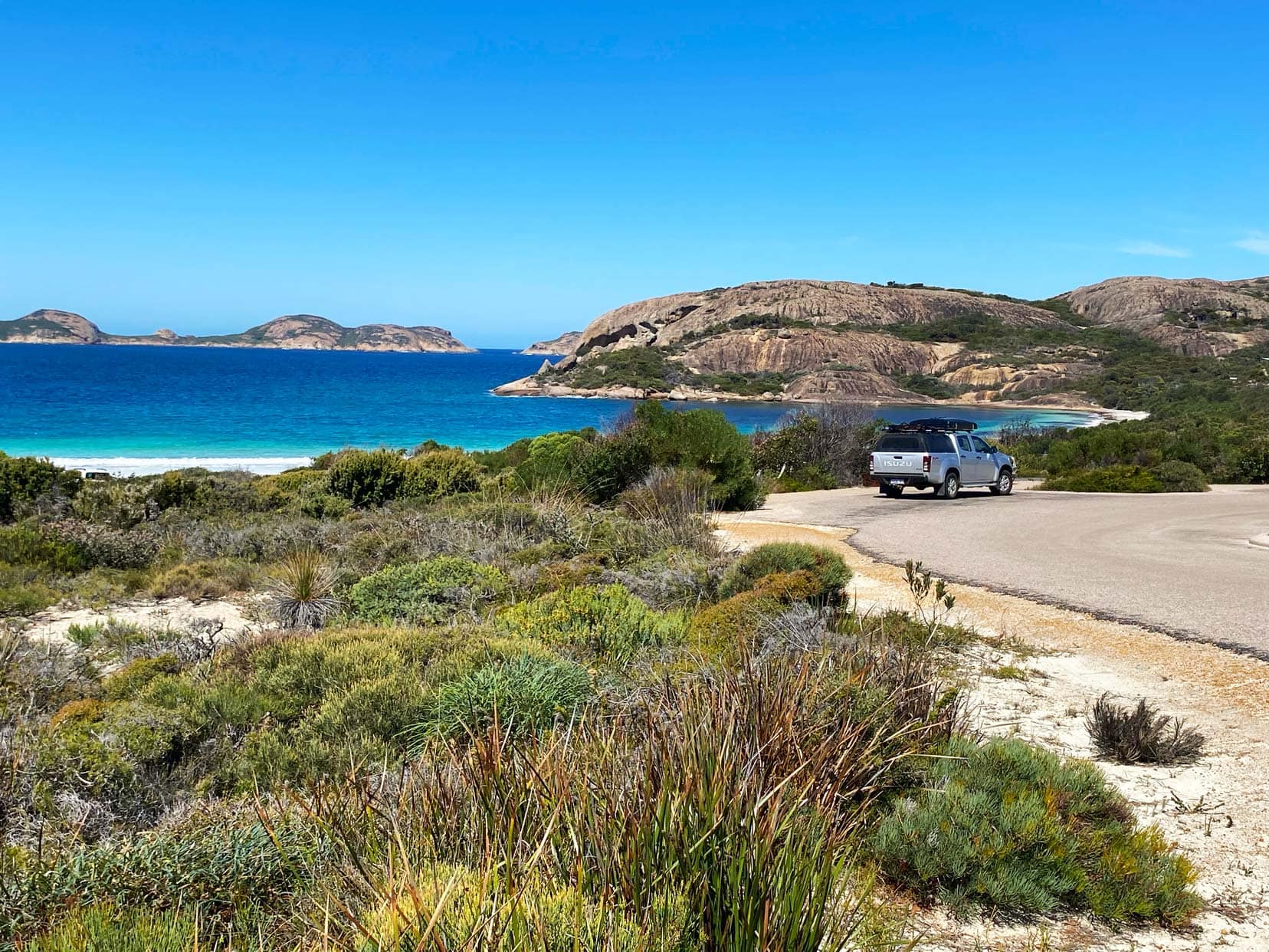 Camping-in-WA-Lucky-Bay-with granite rocks in the ocean and low green shrubs on shore and deep blue turquoise sea