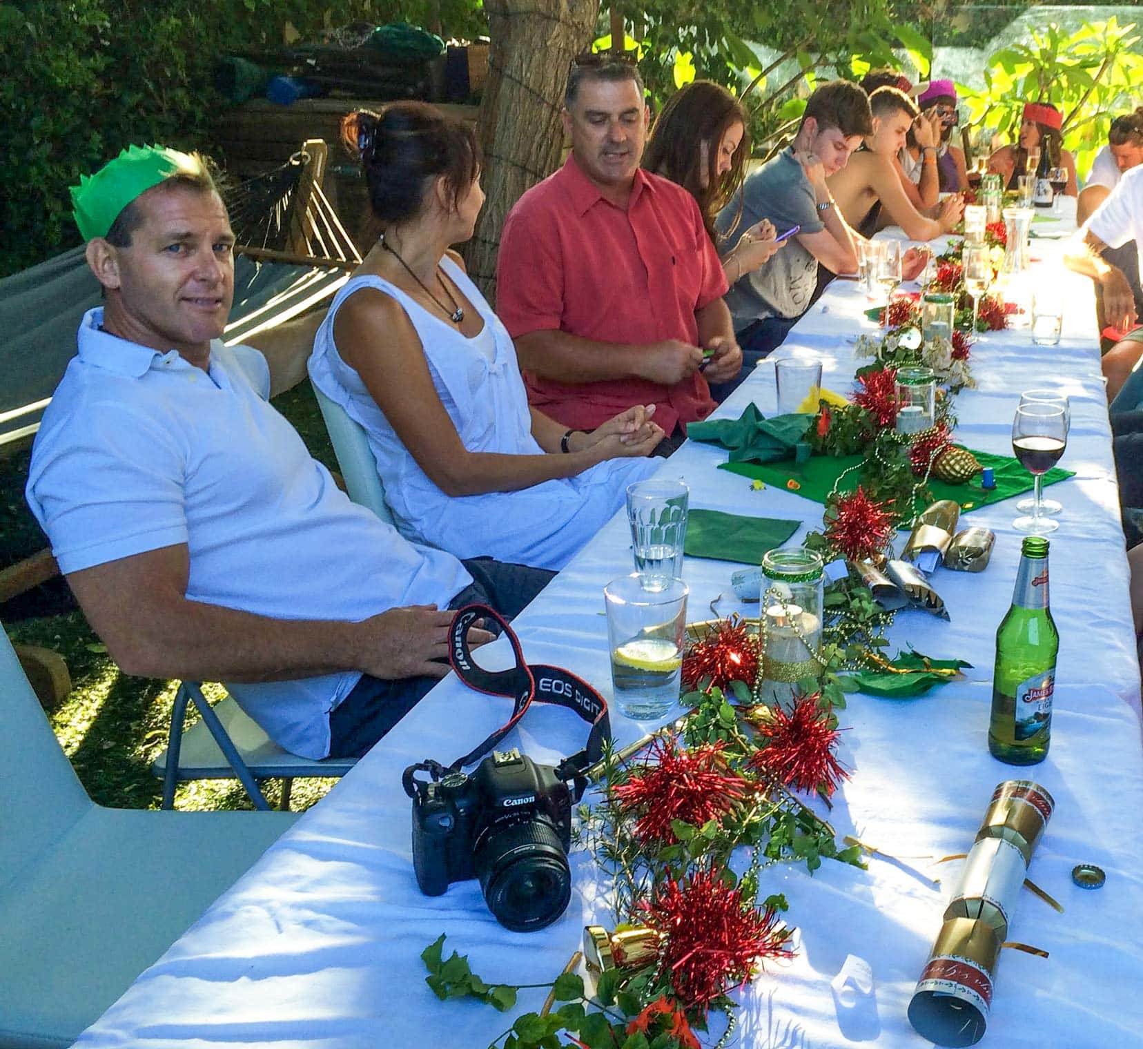 Long table covered with Christmas Decorations and people sat at table outside 