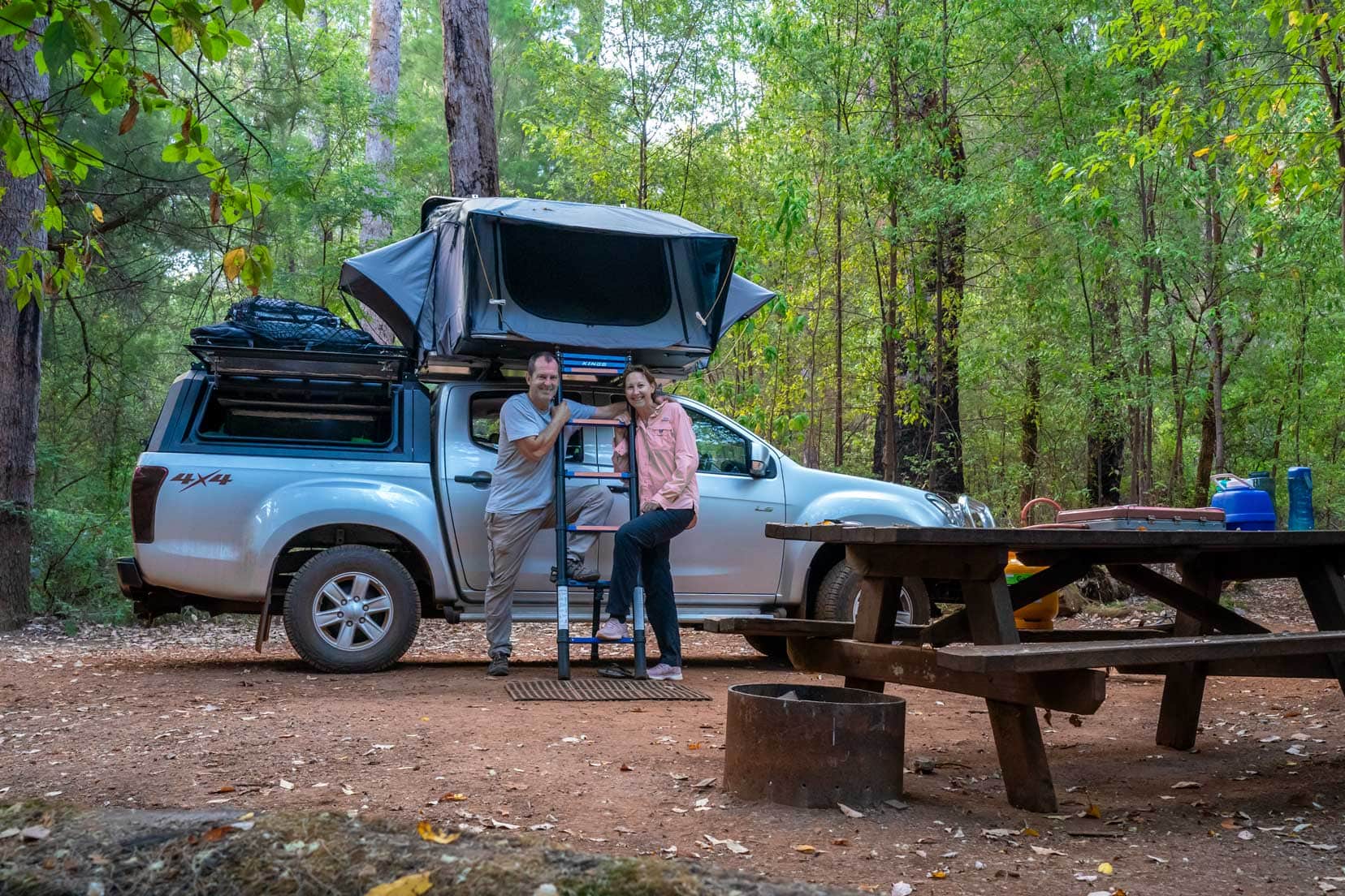 Draftys-Campsite shelley and Lars stood by car with the roof top tent popped open in a forest 